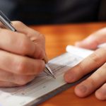 closeup on man`s hands writing a check