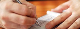 closeup on man`s hands writing a check